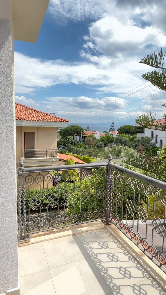 View from a second-floor balcony: wrought-iron railing, the garden, tiled roofs and the sea with mountains in the distance