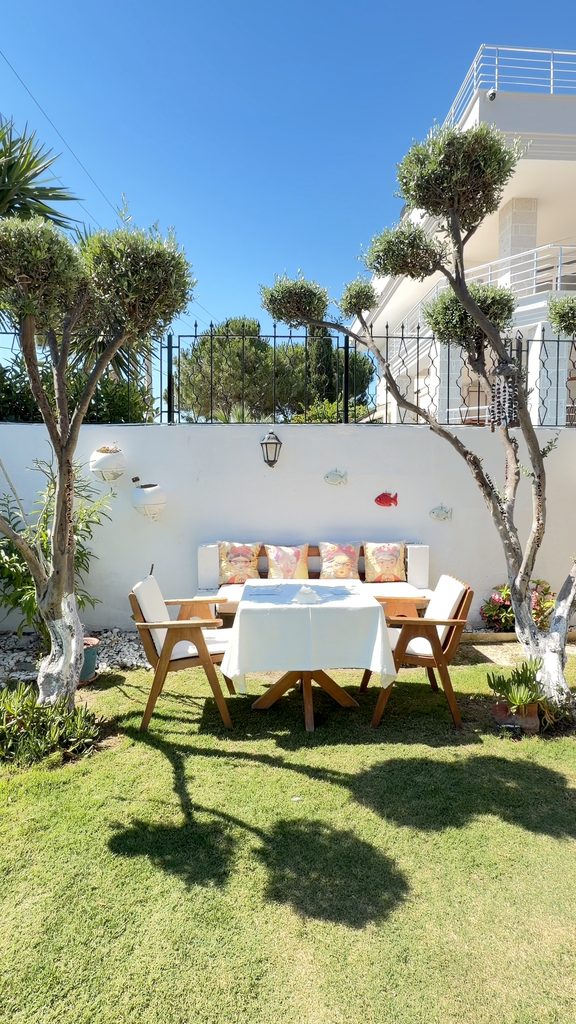 A corner of the garden with olive trees, a white wall and a table for two