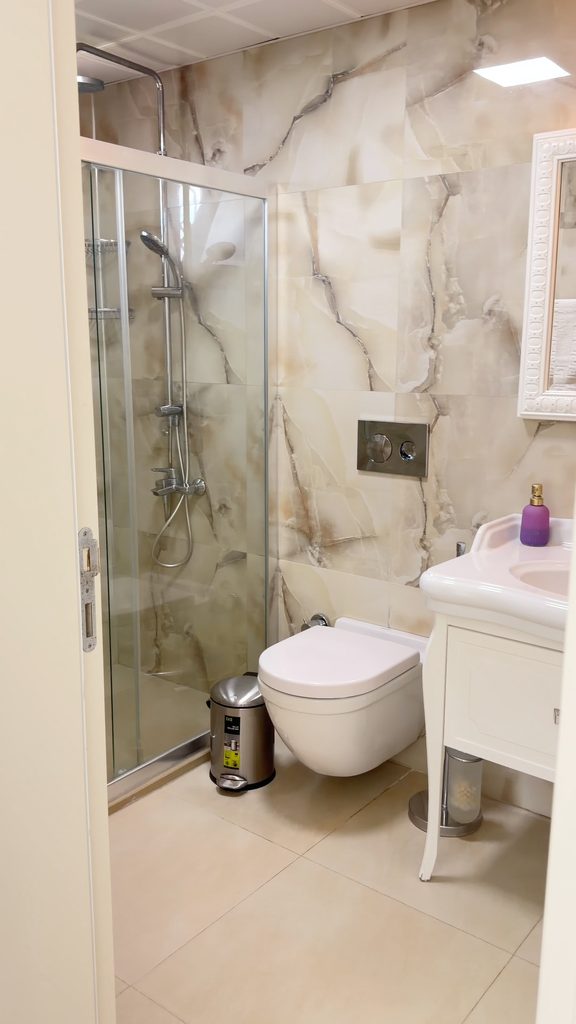 Private bathroom in the room: shower cabin, marble tiles, wall-hung toilet and washbasin