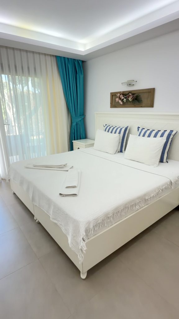 Guest room with a double bed, blue-and-white striped pillows and turquoise curtains